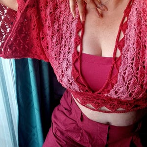 Op de afbeelding: Een rood en roze gehaakt topje met een diepe V-hals en een strik sluiting aan de achterkant. Het topje is gemaakt met een delicaat open steekpatroon.