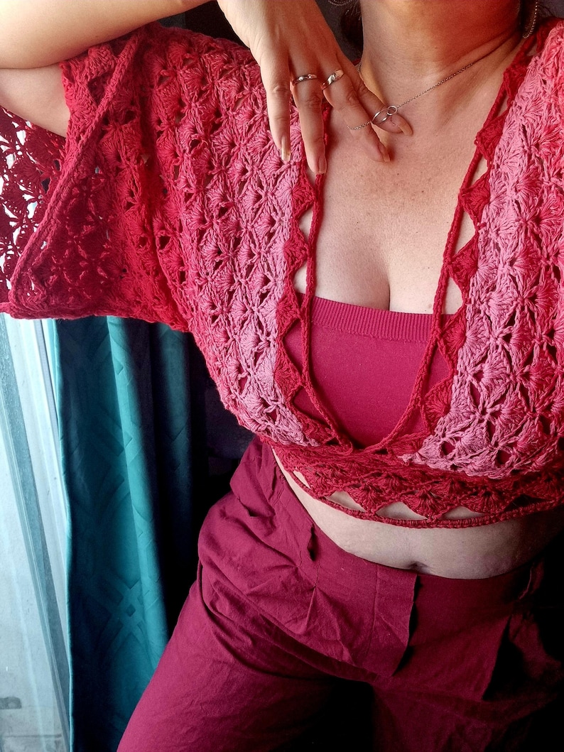 Op de afbeelding: Een rood en roze gehaakt topje met een diepe V-hals en een strik sluiting aan de achterkant. Het topje is gemaakt met een delicaat open steekpatroon.