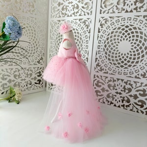May include: A pink tulle dress with a high-low hemline and a satin bodice. The dress has a bow on the back and is decorated with small pink flowers.