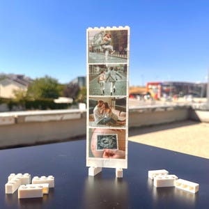 May include: A white Lego brick photo display showing four images of a couple, including an ultrasound scan. The display stands upright on two white Lego brick supports. More white Lego bricks are scattered around the base.