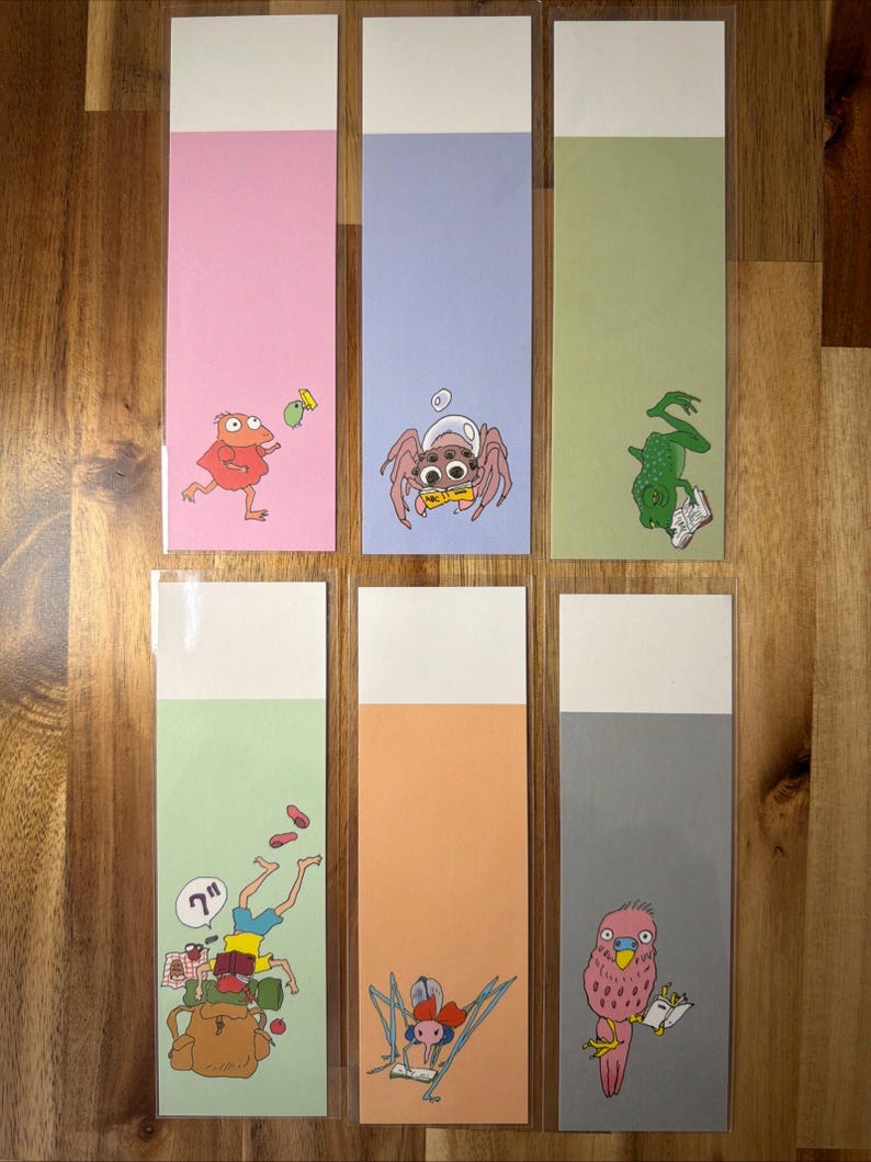 May include: A collection of six illustrated bookmarks. Each bookmark has a different pastel background and features a cartoon character, such as a frog or spider. The top section of each bookmark is white.