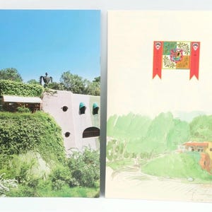 Puede incluir: Dos postales con diseños arquitectónicos y paisajísticos. Una muestra un edificio cubierto de vegetación con una estructura alta en forma de jaula y un cielo azul. La otra representa una ilustración a la acuarela de un paisaje con una bandera.