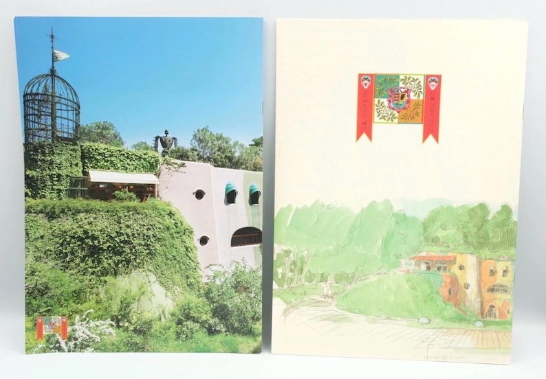 May include: Two postcards featuring architectural and landscape designs. One shows a building covered in greenery with a tall cage-like structure and a blue sky. The other depicts a watercolor illustration of a landscape with a flag.