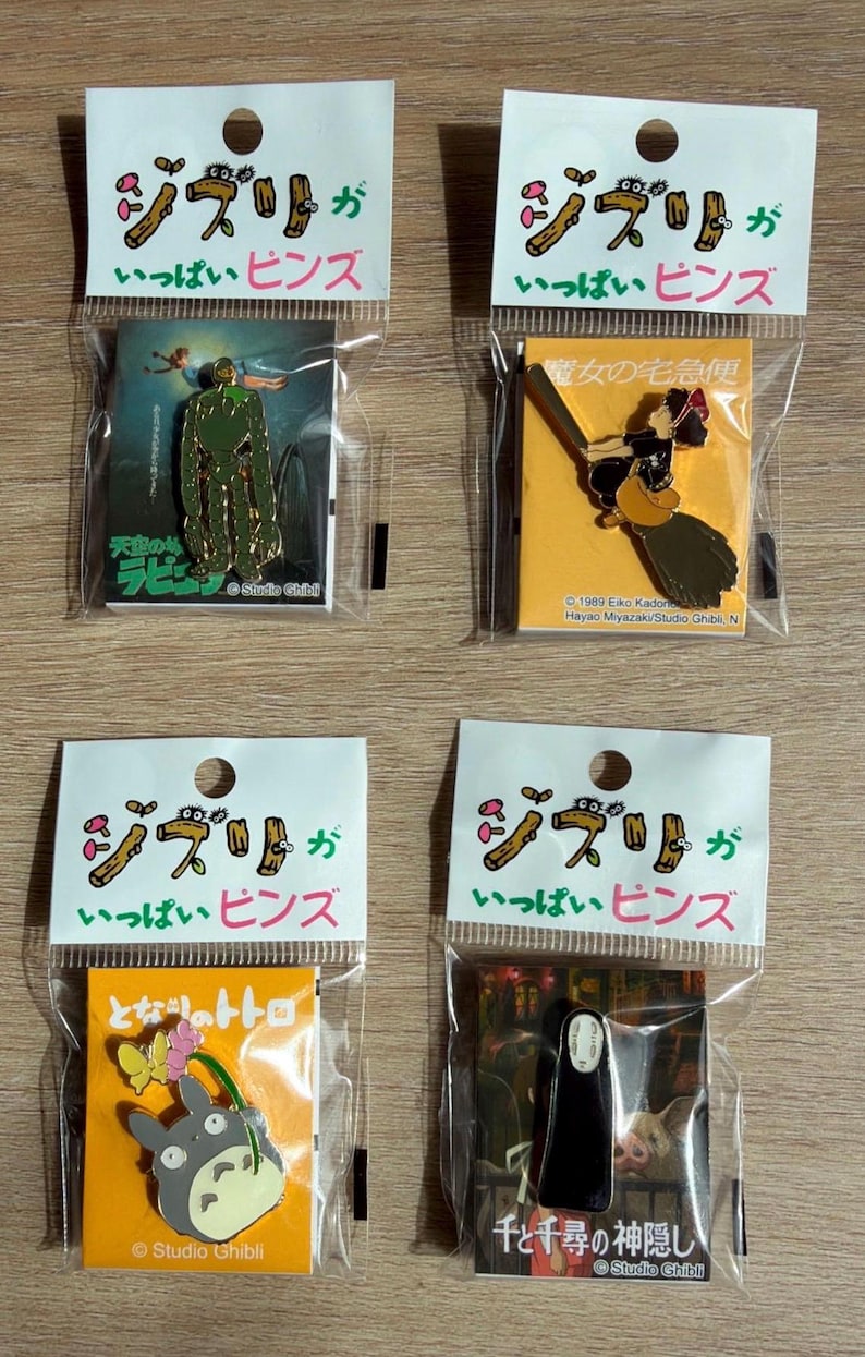 May include: Four Studio Ghibli pins in clear plastic packaging. Each pin features a different character or scene from popular animated films. The packaging includes Japanese text and the Studio Ghibli logo.