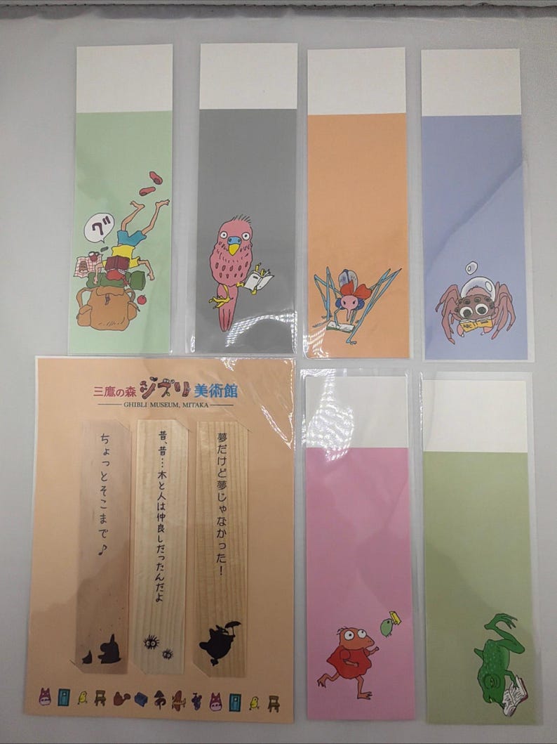 May include: A selection of illustrated bookmarks in various colours, including green, grey, orange, and pink. The bookmarks feature cartoon characters and Japanese text. The bookmarks are from the Ghibli Museum.