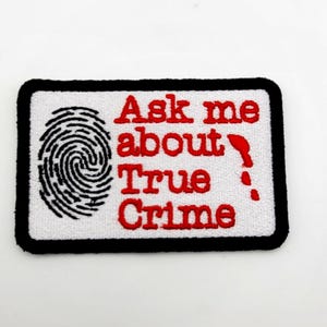 May include: A rectangular embroidered patch with a white background and a thick black border. It features a black fingerprint graphic on the left and the red text "Ask me about True Crime" with a red blood drop graphic on the right side.