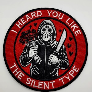 May include: Embroidered patch with a red circular border and the text "I HEARD YOU LIKE THE SILENT TYPE". The patch features a black and white illustration of a figure in a hoodie holding roses and a knife.