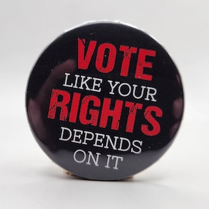 May include: Black button with white text that reads "Vote Like Your Rights Depends On It". The word "Vote" is in red and the rest of the text is in white.