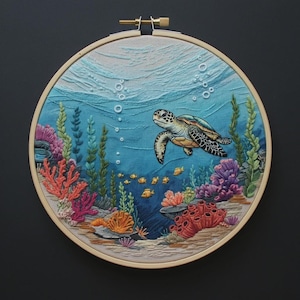 May include: A circular embroidery hoop containing a detailed fabric scene of an underwater environment. A sea turtle swims through blue water with white bubbles, surrounded by vibrant orange, pink, and purple coral reefs and green seaweed.