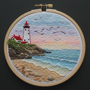 Puede incluir: Un bastidor de bordado circular con una escena costera cosida a mano. El diseño muestra un faro blanco con techo rojo, acantilados rocosos, una playa de arena con pequeñas piedras, olas azules y aves volando en un cielo de atardecer.