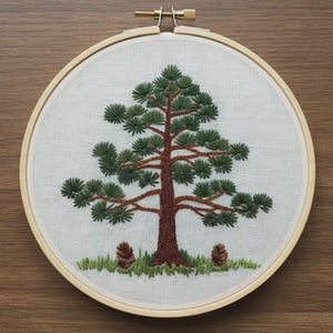 Può includere: Opera d'arte ad albero ricamata in un cerchio di legno. L'albero presenta un tronco e rami marroni con aghi verdi. Due pigne marroni si trovano alla base dell'albero, con erba verde. Lo sfondo è in tessuto bianco.