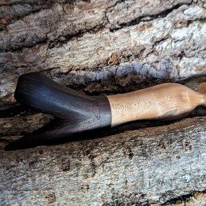 Pode incluir: Um abridor de garrafas de madeira artesanal. O abridor apresenta uma pega bifurcada castanha escura e um corpo castanho claro. As duas cores de madeira são separadas por uma faixa castanha escura. O abridor é exibido numa superfície castanha texturizada.