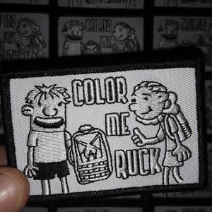 May include: A black and white embroidered patch with the text "Color Me Ruck" and two cartoon figures. The figures are wearing backpacks and one is giving a thumbs up.