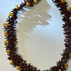 May include: A necklace and matching bracelet set. The necklace and bracelet are made of dark brown, leaf-shaped beads and interspersed with yellow, shell-shaped beads. The necklace has a gold-colored clasp.