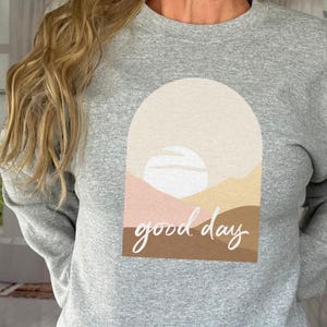 May include: A gray sweatshirt with a graphic design of a sunset with the text "good day" in white.