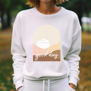 May include: White sweatshirt with a graphic design of a sunset with the text "good day" in brown and beige.