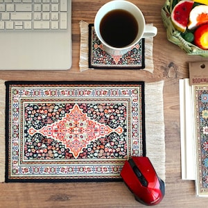 May include: A desk setup featuring a small rug-style mousepad, a matching coaster with a coffee cup, and a bookmark. The items have a black background with a red and floral design. A red mouse and a laptop are also present.