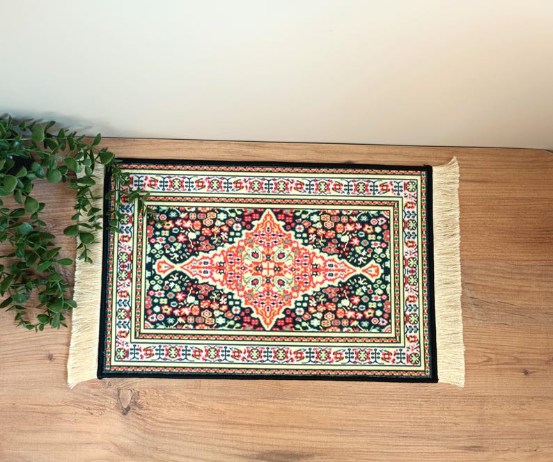 Pode incluir: Um tapete decorativo retangular com borda preta e franjas creme. O tapete apresenta um design central em forma de diamante em vermelho e creme, rodeado por um padr&atilde;o floral em v&aacute;rias cores.