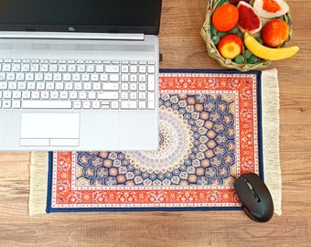 May include: A blue and red patterned mouse pad with a fringe border. The mouse pad is on a wooden surface with a laptop and a bowl of fruit.