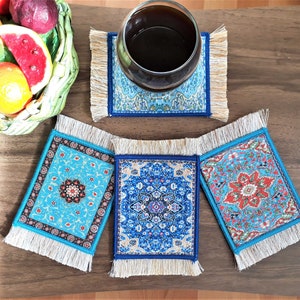 May include: Four blue and white patterned coasters with fringe trim. The coasters feature intricate floral designs and are perfect for protecting surfaces from heat and spills.