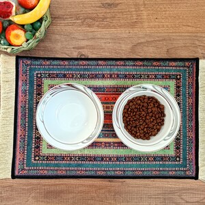 May include: Two white ceramic bowls on a colorful patterned rug. One bowl is empty, and the other is filled with brown dog food.
