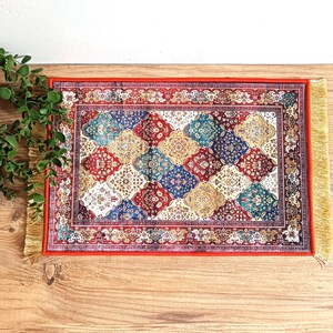 May include: A red, blue and gold patterned rug with a fringed border. The rug has a geometric design with diamond shapes.