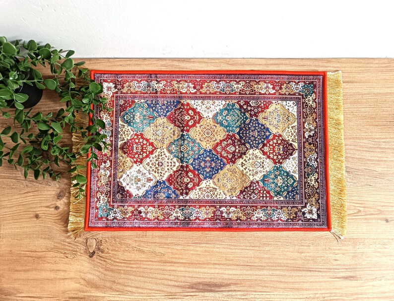 May include: A red, blue and gold patterned rug with a fringed border. The rug has a geometric design with diamond shapes.
