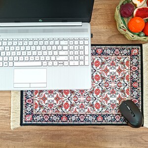 May include: A laptop computer sits on a white and red patterned mouse pad with a black computer mouse on the right side. The mouse pad has a fringe border.