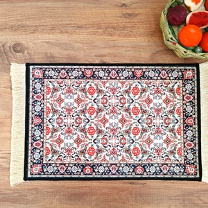 May include: A small, rectangular rug with a white background and a black, red, and cream floral pattern. The rug has fringe on all four sides.