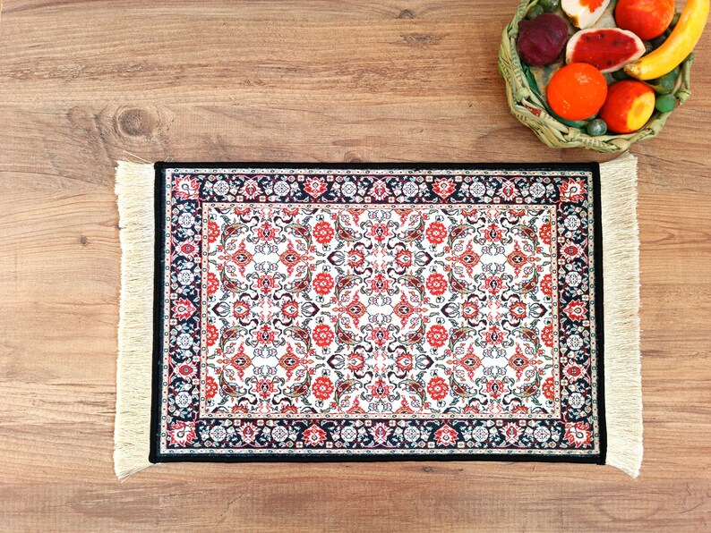 May include: A small, rectangular rug with a white background and a black, red, and cream floral pattern. The rug has fringe on all four sides.