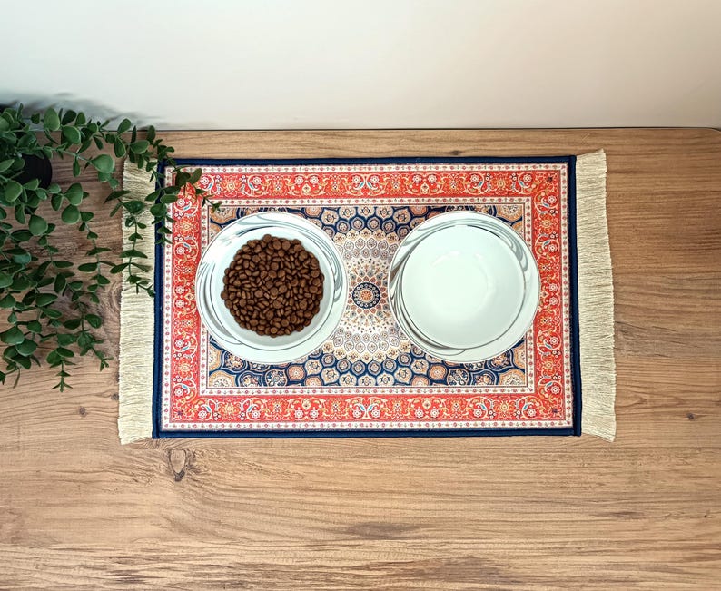 May include: A blue and red patterned rug with fringe, featuring two white bowls. One bowl contains brown pet food.