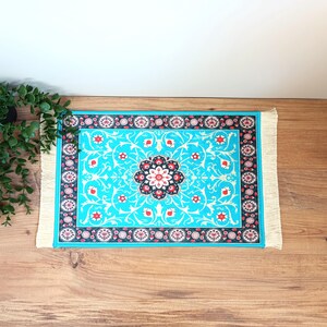 Peut inclure: Un tapis bleu et blanc &agrave; motifs floraux avec une bordure en frange blanche. Le tapis est pos&eacute; sur une surface en bois.