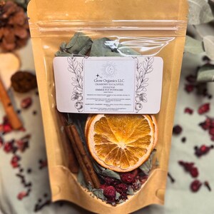 May include: A brown paper bag with a clear plastic window showing a mix of dried fruit, spices, and herbs. The bag is labeled "Grow Organics LLC Cranberry Eucalyptus Stovetop Simmer Pot Potpourri".