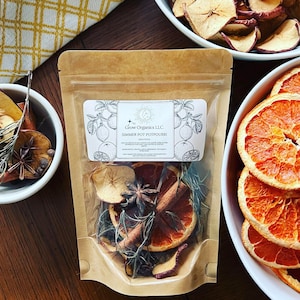 May include: A brown paper bag with a clear window showing a simmer pot potpourri mix. The mix includes orange slices, cinnamon sticks, star anise, apple slices, and rosemary. The bag has a label that reads "Grow Organics LLC Simmer Pot Potpourri".