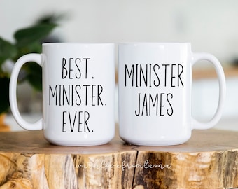May include: Two white ceramic mugs with black text. One mug says "Best. Minister. Ever." and the other mug says "Minister James".