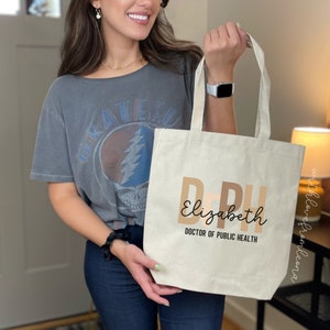 May include: A beige canvas tote bag with the text "DPH Elizabeth Doctor of Public Health" printed in brown and black.