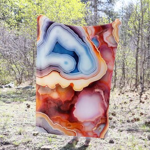 May include: A colorful throw blanket with a large agate pattern in shades of red, orange, yellow, blue, and white. The blanket is made of soft, plush fabric and is perfect for adding a touch of nature to your home decor.