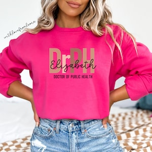May include: Pink sweatshirt with the text "DrPH Elizabeth DOCTOR OF PUBLIC HEALTH" in brown and beige letters.