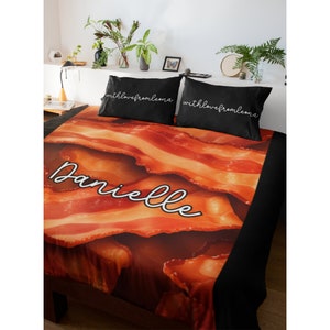 May include: A black and orange bedding set with a bacon print and the name "Danielle" written in white cursive. The pillowcases have the text "with love from Leona" written in white cursive.