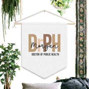 May include: White banner with brown text that reads "DrPH Morgan DOCTOR OF PUBLIC HEALTH". The banner is hanging from a white rope.