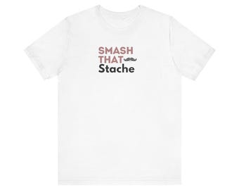 May include: White t-shirt with the text "SMASH THAT Stache" in black and pink lettering with a small black mustache graphic.