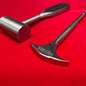 May include: A metal mallet with a cylindrical head and a smooth handle alongside a metal tool with a curved, fan-shaped head featuring the word FREEMAN engraved on the surface. Both tools have a polished, reflective finish and metallic texture.