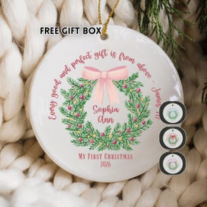May include: A white ceramic Christmas ornament with a wreath design and a pink bow. The ornament has the text "Every good and perfect gift is from above" and "My First Christmas 2026". The name "Sophia Ann" is also displayed.