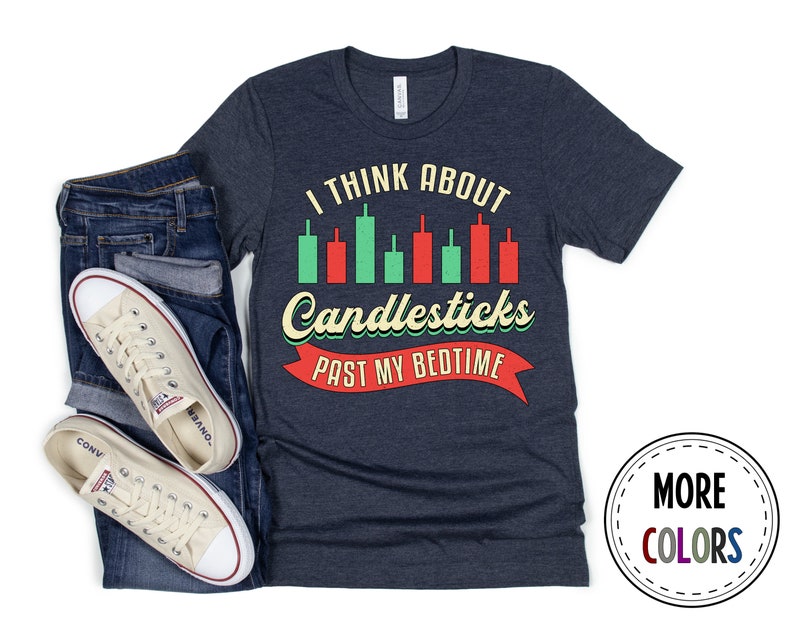 以下が含まれることがあります： ヴィンテージスタイルのフォントで「I think about candlesticks past my bedtime」と書かれたネイビーブルーのTシャツ。テキストは赤いリボンとキャンドルスティックチャートのグラフィックで囲まれています。