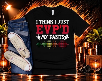 May include: A black short-sleeved t-shirt featuring the white and red text I THINK I JUST EVP'D MY PANTS, accompanied by two small white ghost icons and a colorful sound wave graphic in green, yellow, and red dots, paired with blue jeans.