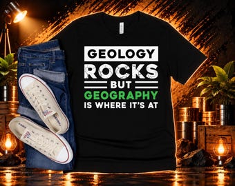 May include: A black short-sleeve t-shirt featuring the white and green text GEOLOGY ROCKS BUT GEOGRAPHY IS WHERE IT'S AT, paired with blue denim jeans and a pair of off-white canvas sneakers with white laces and rubber soles.
