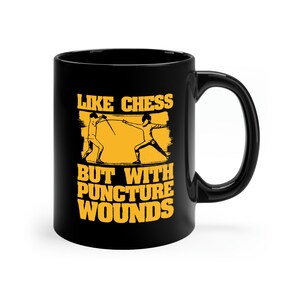 May include: Black ceramic mug with a white interior. The mug features a yellow and black graphic of two fencers and the text "LIKE CHESS BUT WITH PUNCTURE WOUNDS" in yellow.