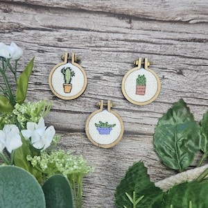 Ensemble de 3 mini modèles de broderie au point de croix représentant des plantes en pot : aloès, cactus et sansevieria.