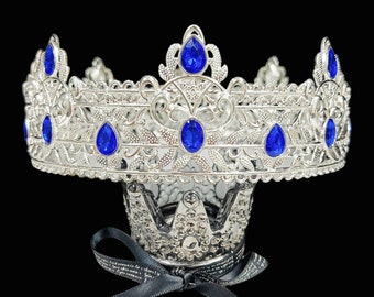 May include: Silver crown with blue gem accents. The crown has a delicate, ornate design and is perfect for a costume or theatrical performance.