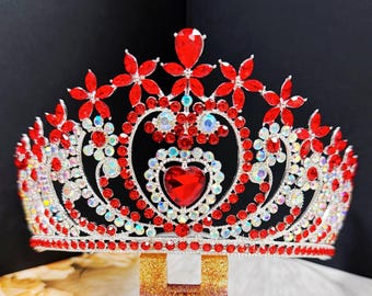 May include: A silver-toned crown with red and clear gemstones. The crown features a heart-shaped centerpiece and floral accents. The gemstones are arranged in a symmetrical pattern, creating a sparkling and elegant design.